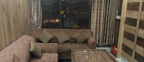 A modern living room with a brown sectional sofa, a matching ottoman, and a large window with curtains.