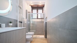 Ein modernes Badezimmer mit Waschtisch aus Holz, zwei Toiletten, einer Duschkabine aus Glas und einem großen Spiegel mit Beleuchtung.