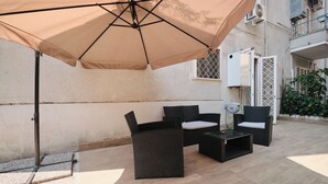 Ein Terrassenbereich im Freien mit einem beige farbenen Sonnenschirm, Korbmöbeln und einem gefliesten Boden.