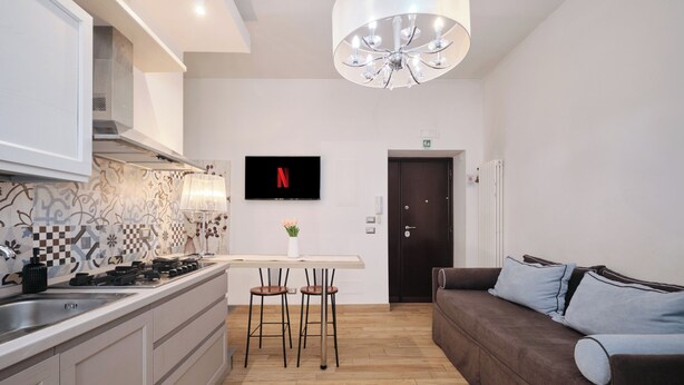 Eine moderne Küche mit einer zentralen Kochinsel, einem Essbereich mit Stühlen, einer Couch und einem an der Wand befestigten Fernseher.