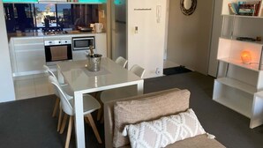 A modern kitchen with white cabinets, a dining table with chairs, and a cozy seating area with a bench and cushions. - Circle on Cavill - Ocean-View Apartment (Surfers Paradise)