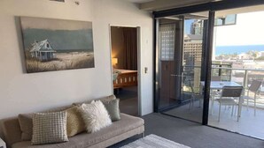 A modern living room with a beige sofa, a white coffee table, and a painting of a beach house. - Circle on Cavill - Ocean-View Apartment (Surfers Paradise)