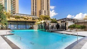 A swimming pool with a clear blue water, surrounded by a tiled deck and a covered area with lounge chairs. - Circle on Cavill - Ocean-View Apartment (Surfers Paradise)