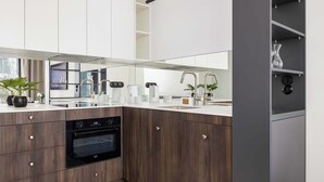 A modern kitchen with wooden cabinets, a built-in oven, a sink, and a countertop with various appliances and decorative items. - Comfortable Studio near Arena | Parking in Garage (Kraków)