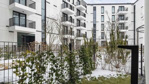 A modern apartment building with balconies, a fenced garden area, and a snow-covered ground. - Comfortable Studio near Arena | Parking in Garage (Kraków)