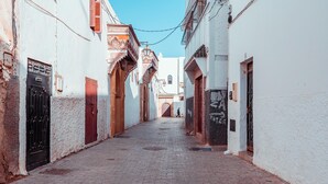 Una estrecha calle adoquinada flanqueada por edificios blancos con puertas y ventanas rojas, que conduce a un arco a lo lejos.