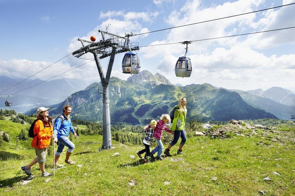 Un grupo de personas caminando por un sendero de montaña, con un teleférico al fondo.