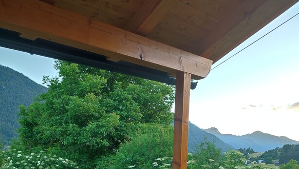 Un espace extérieur abrité, aménagé pour les repas, avec une table et des chaises, offrant une vue sur un paysage montagneux et une végétation luxuriante.