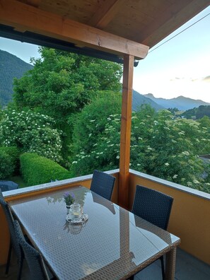 Área de refeições coberta ao ar livre, com mesa e cadeiras, com vista para uma paisagem montanhosa e vegetação exuberante.