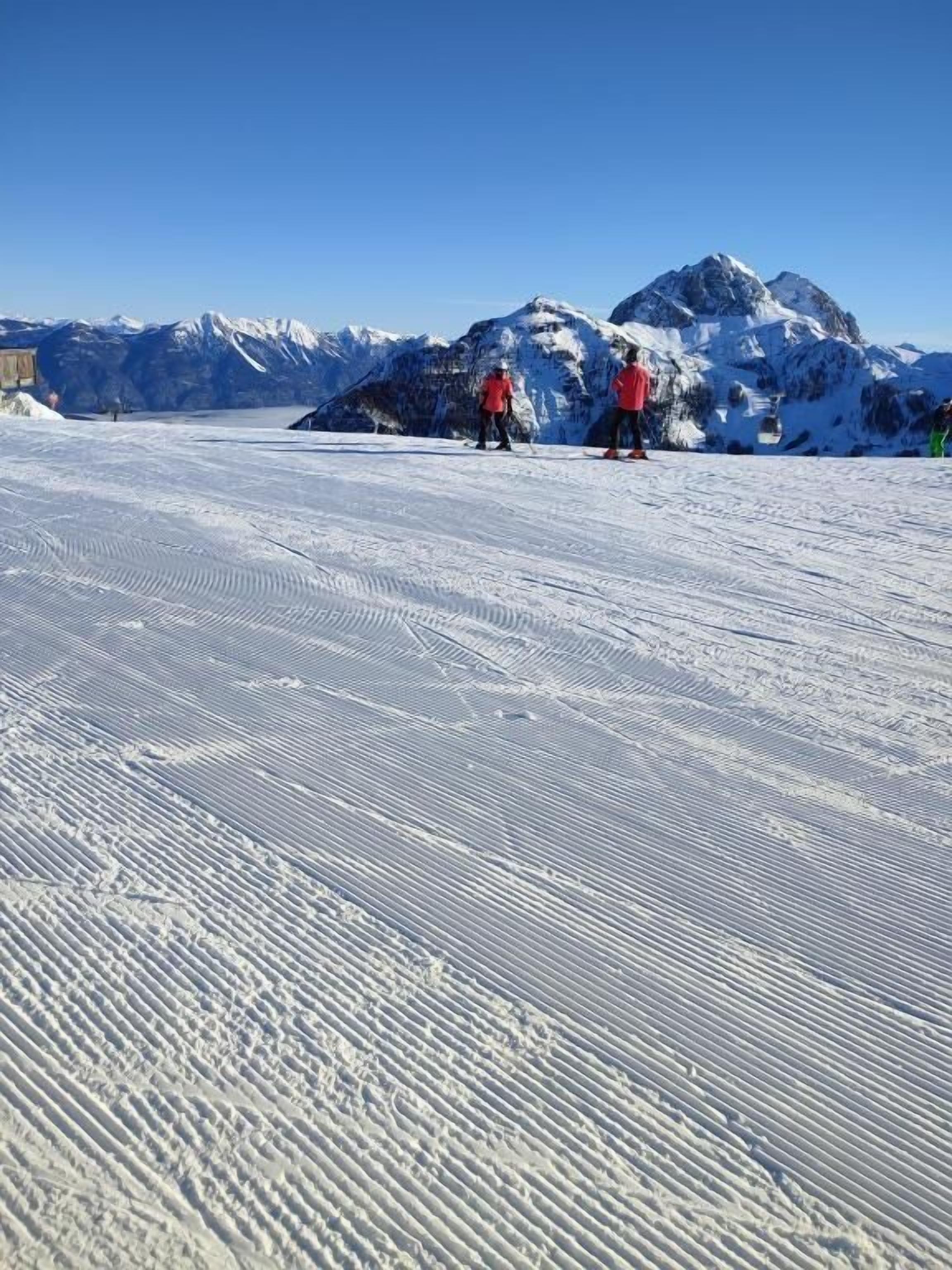 Ein verschneiter Skipisten mit zwei Skifahrern in roten Jacken.