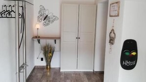 Un couloir avec un plafond en bois, un étagère en métal, une décoration murale représentant des papillons, une porte blanche, un tableau encadré et une pancarte « Bienvenue à la maison ».