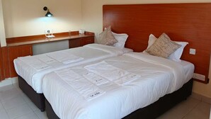 Un letto matrimoniale con lenzuola bianche e due cuscini, una testiera in legno, un comodino con una lampada e un punto luce a parete.