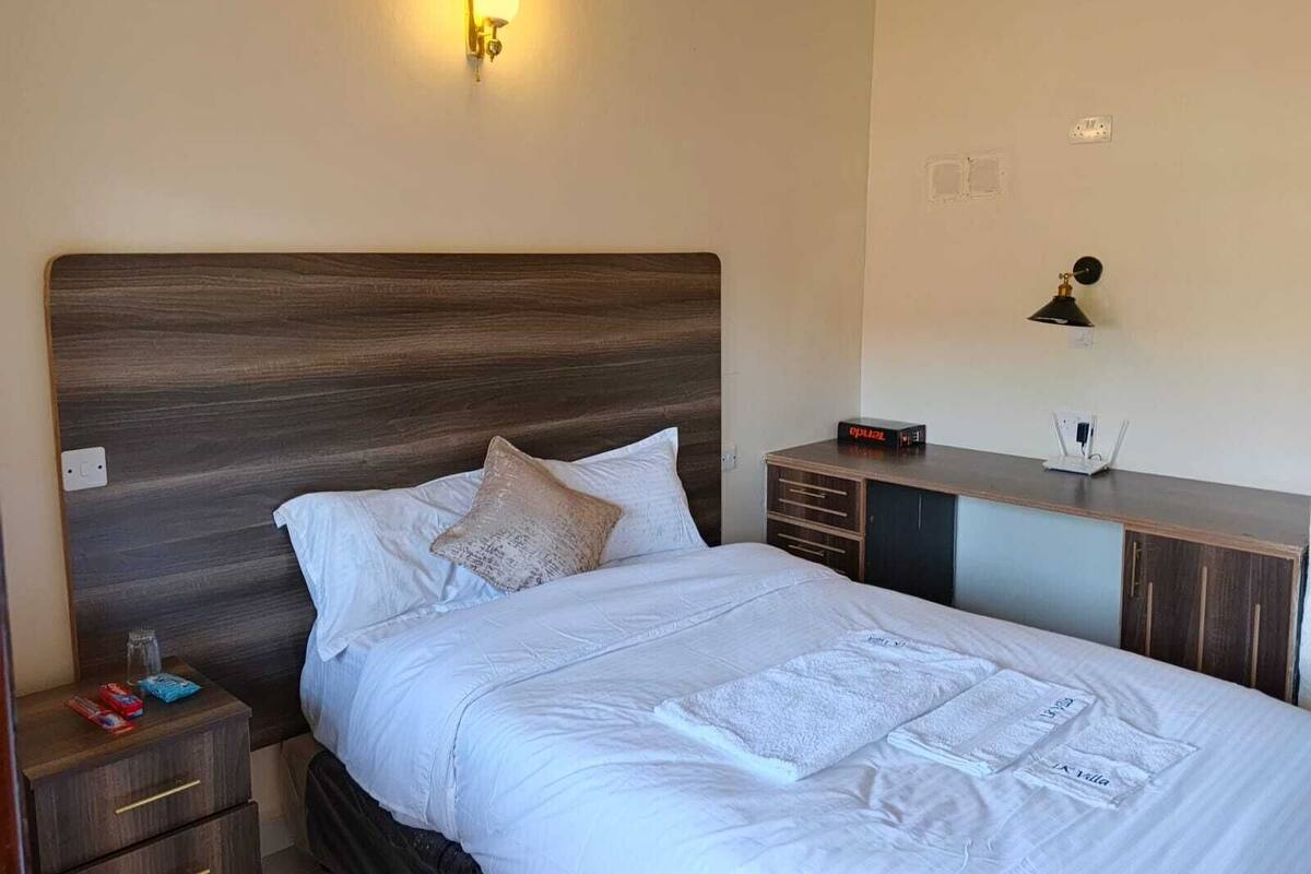 A neatly made bed with white linens, a wooden headboard, and a bedside table with a lamp and a clock.