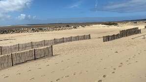 Een zandstrand met een houten omheining, voetafdrukken en een verafgelegen vuurtoren.