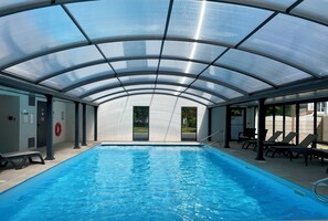 Una piscina techada con paneles de vidrio transparente, sillas de descanso y un flotador en la pared.