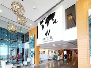 A modern lobby with a large Pacific Al Marjan Island sign, glass walls, and contemporary lighting fixtures. - Pacific Sunset Duplex (Jazeerat Al Marjan)