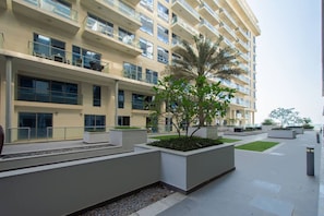 A modern multi-story building with balconies, a landscaped courtyard, and a palm tree. - Pacific Sunset Duplex (Jazeerat Al Marjan)