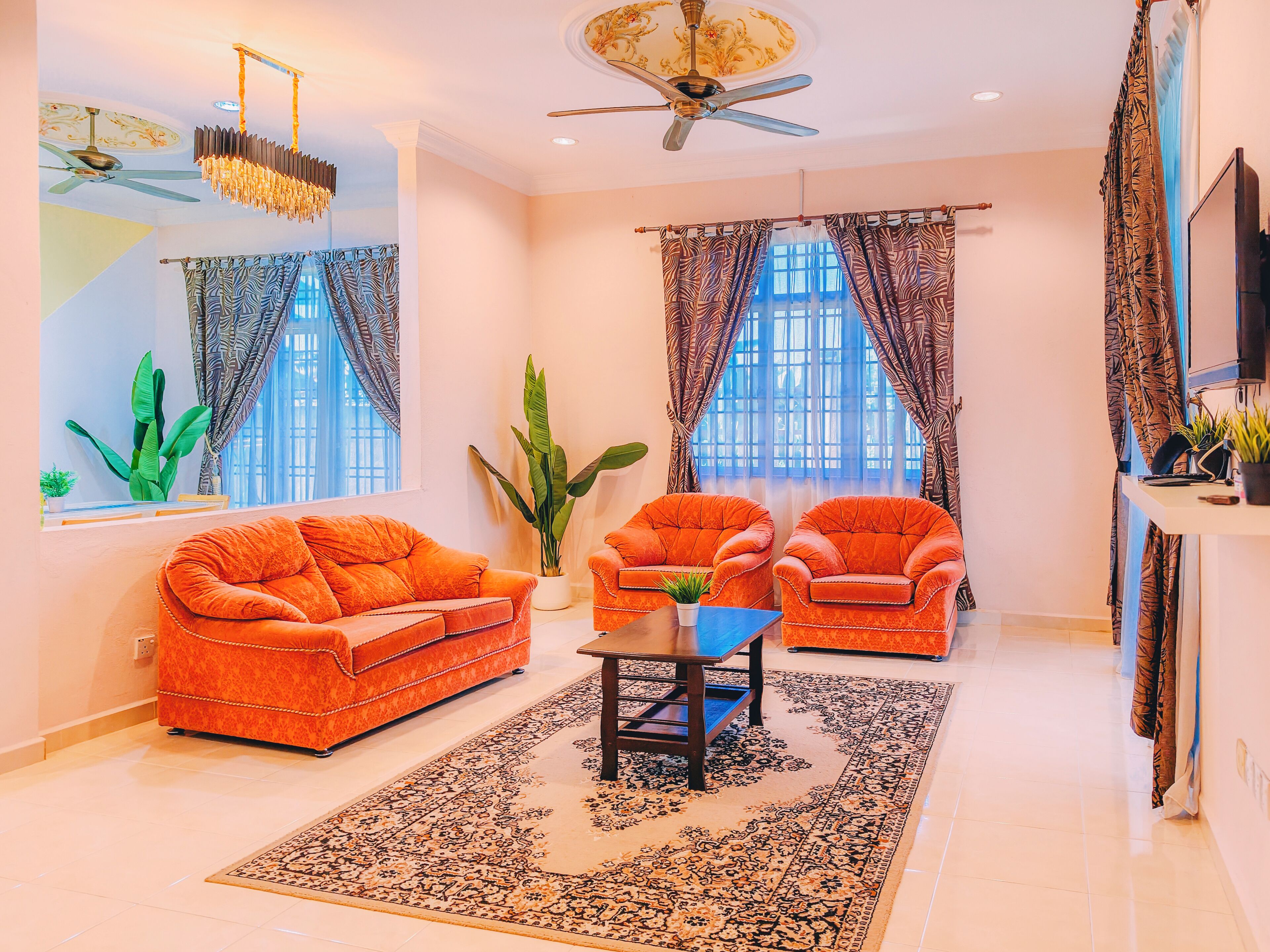 A living room with a sofa, armchairs, a coffee table, a large plant, and a ceiling fan.