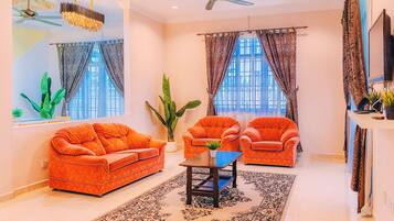 A living room with a sofa, armchairs, a coffee table, a large plant, and a ceiling fan.