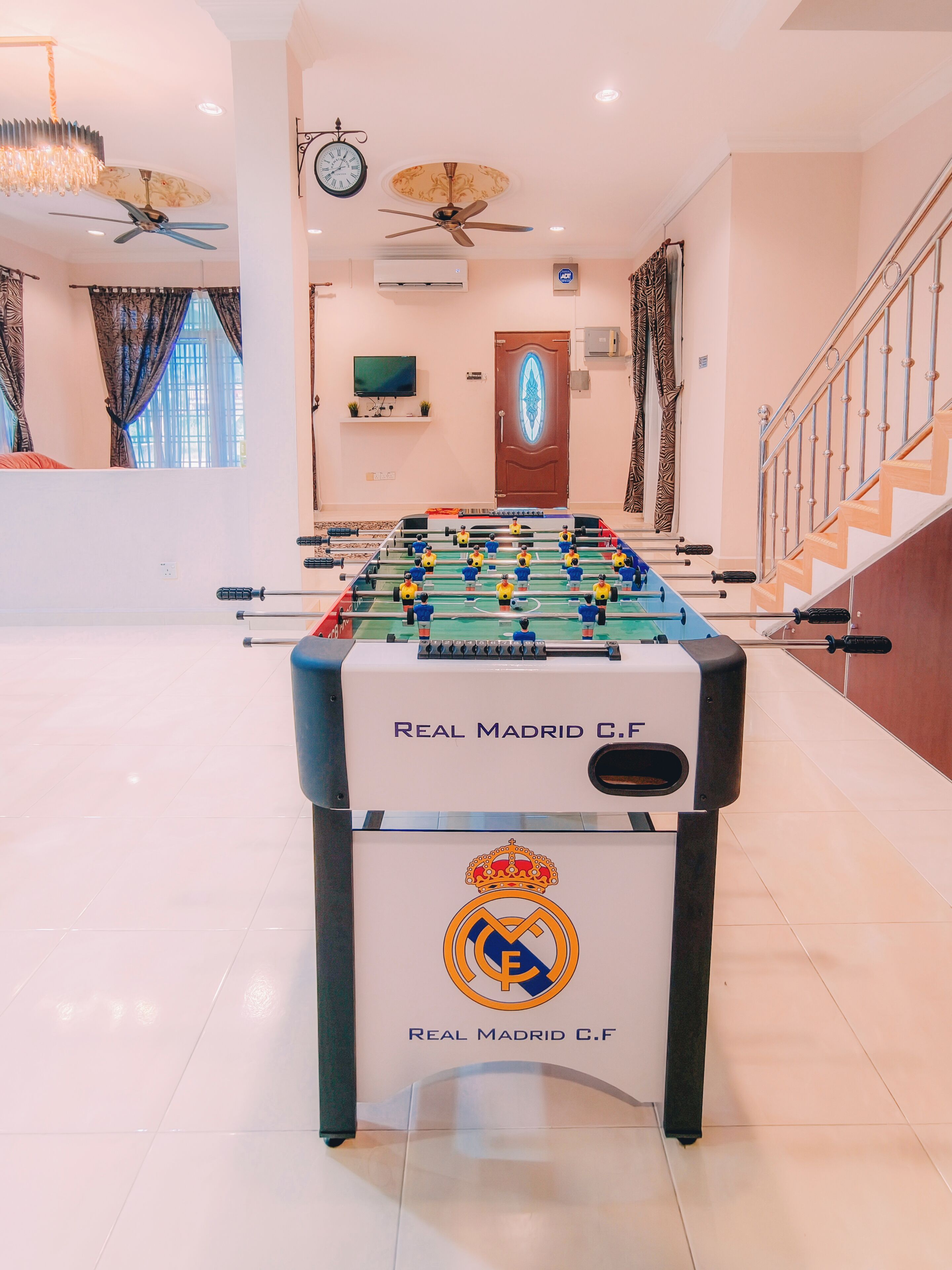 Taula de futbolí amb el logotip del Reial Madrid C.F., una televisió i una escala en una habitació ben il·luminada.