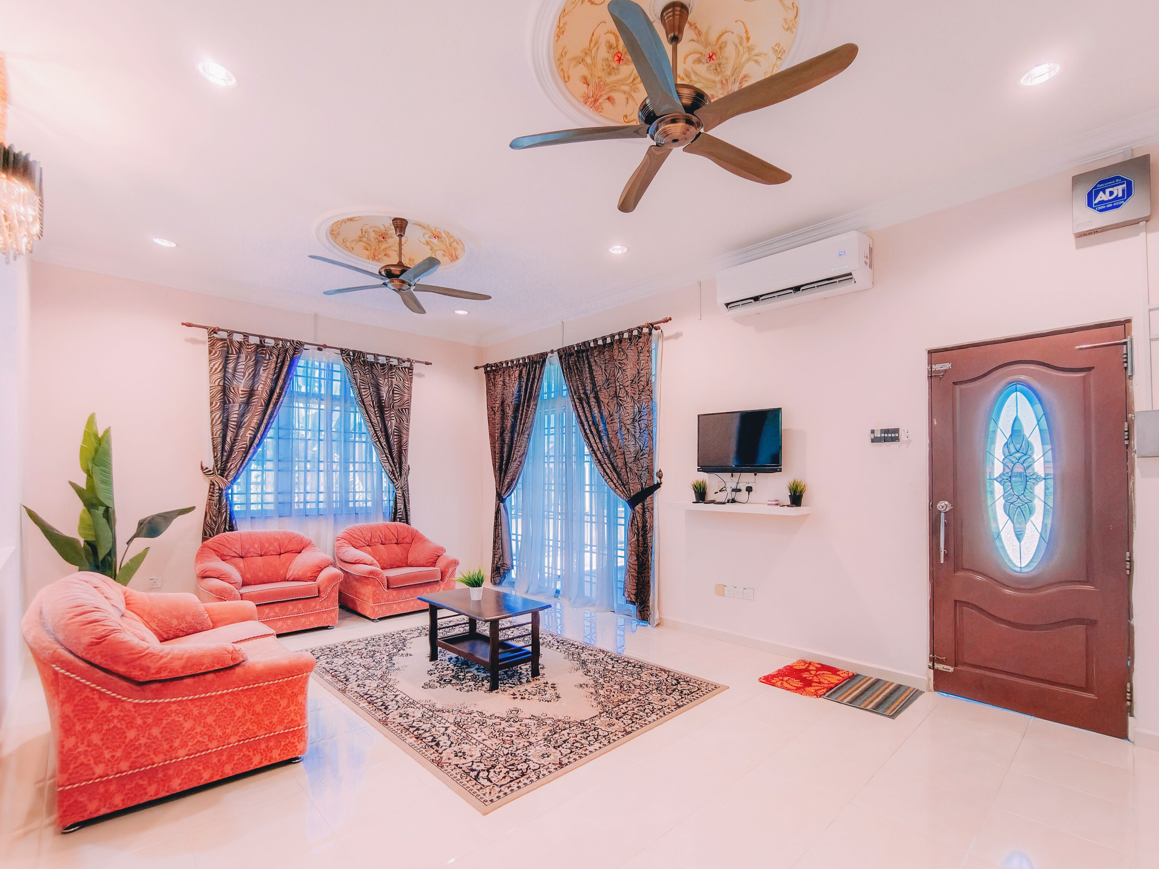 A living room with two sofas, a coffee table, a TV, ceiling fans, and a door with a decorative glass panel.