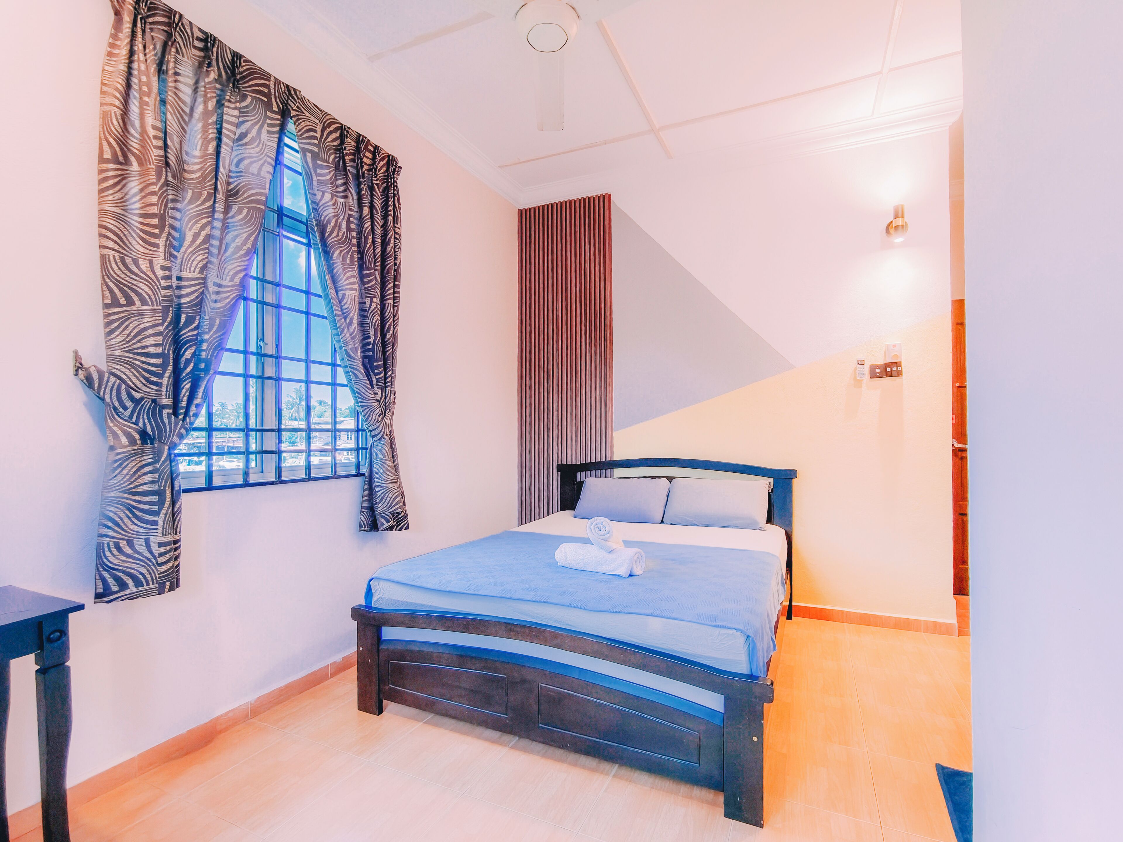 Een slaapkamer met een bed, raam, gordijnen en een wandlamp.