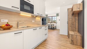 Eine moderne Küche mit weißen Schränken, einer Holz Arbeitsplatte und einem eingebauten Backofen. Auf der Arbeitsplatte steht eine Obstschale und ein Fenster lässt Tageslicht herein.