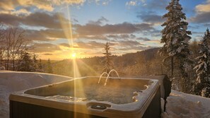 A hot tub in a snowy landscape with a sunset in the background.