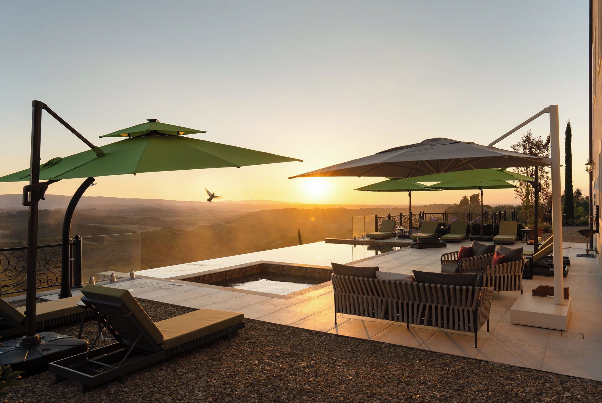 Una terrazza sul tetto con piscina, poltrone a sdraio e ombrelloni, affacciata su un panorama mozzafiato al tramonto.