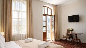 Quarto de hotel com cama, escrivaninha, cadeira, televisão e janela com cortinas.