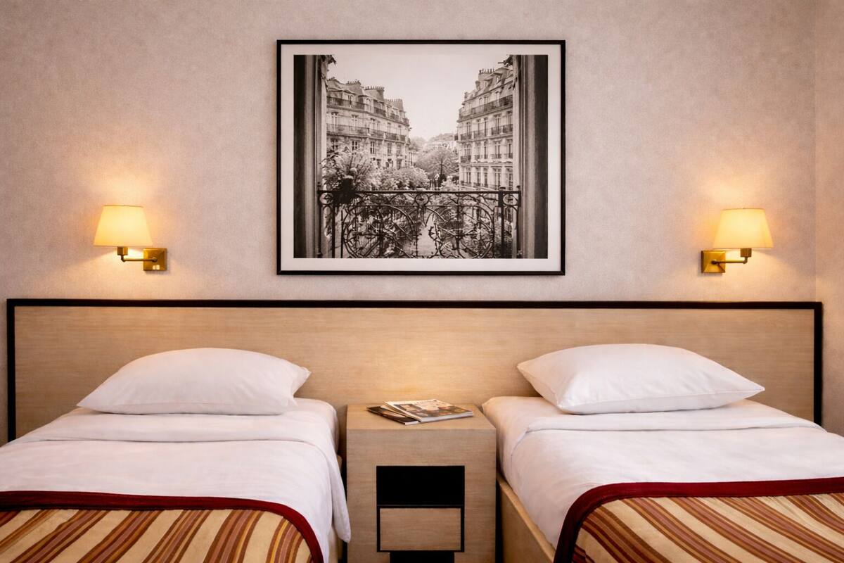 A hotel room with two beds, a framed cityscape picture, and wall-mounted lamps.