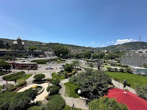 A cityscape with a roundabout, greenery, and a large building with a tower. - Rike Park Hoel (Tbilisi)