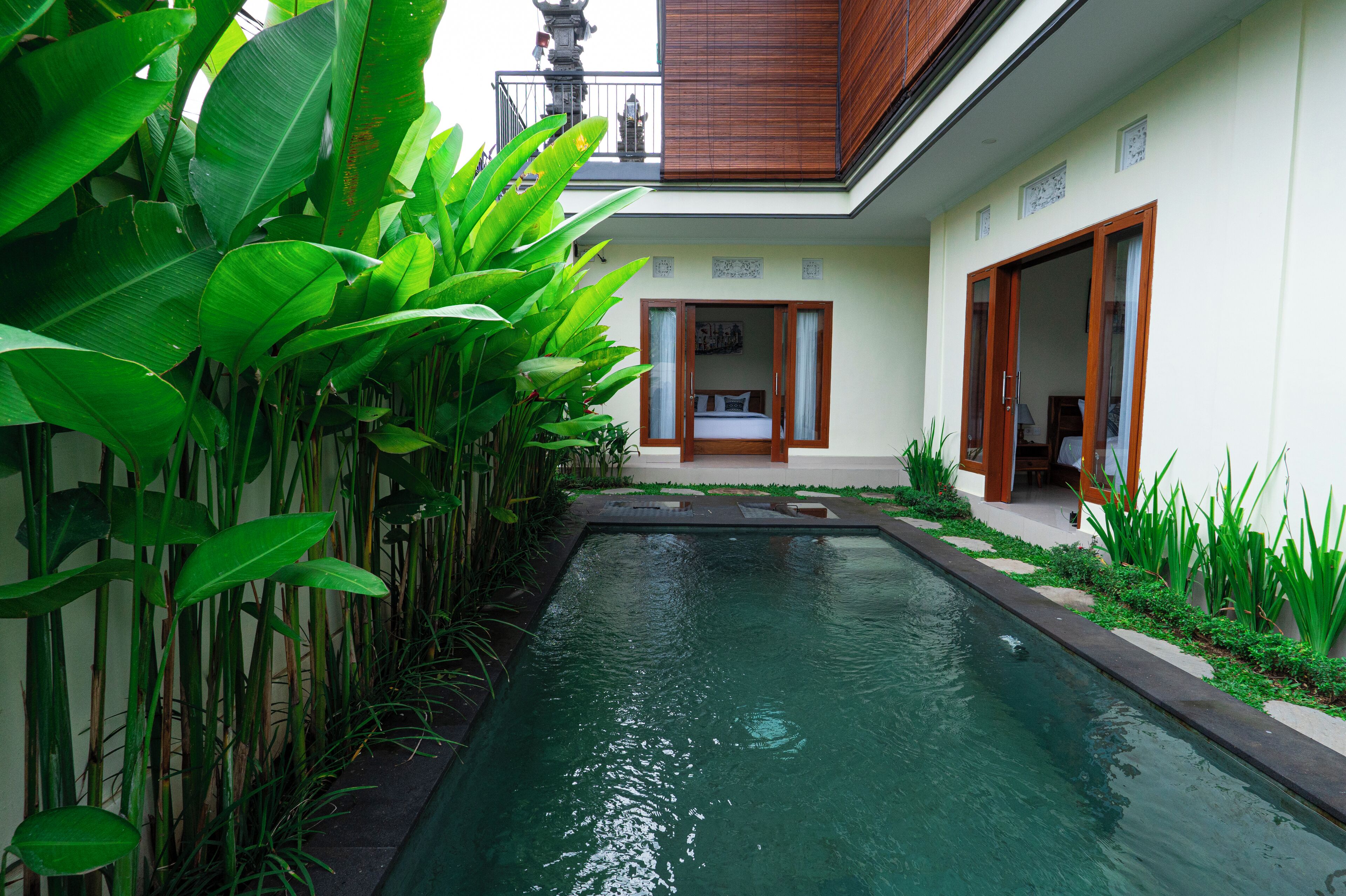 A serene pool area with lush greenery, a wooden deck, and a traditional Balinese architectural style.