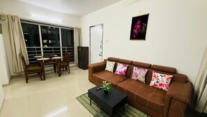 A living room with a brown sofa, a black coffee table, and a dining area with a table and chairs. - 2BHK Service Apart 1703 Parel by Florastays (Mumbai)