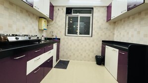 A kitchen with purple cabinets, a gas stove, a window, and a trash bin. - 2BHK Service Apart 1703 Parel by Florastays (Mumbai)