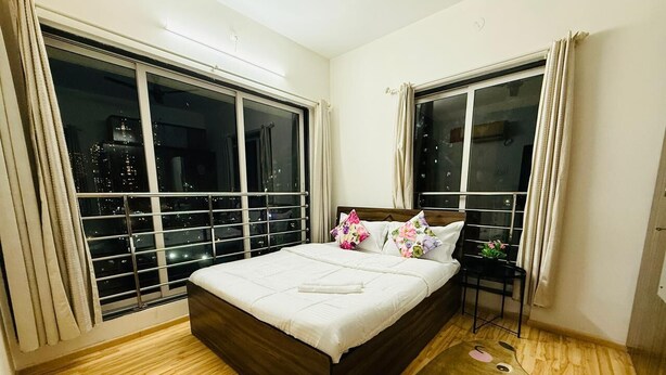 A bedroom with a large bed, two windows, and a view of the city at night. - 2BHK Service Apart 1703 Parel by Florastays (Mumbai)