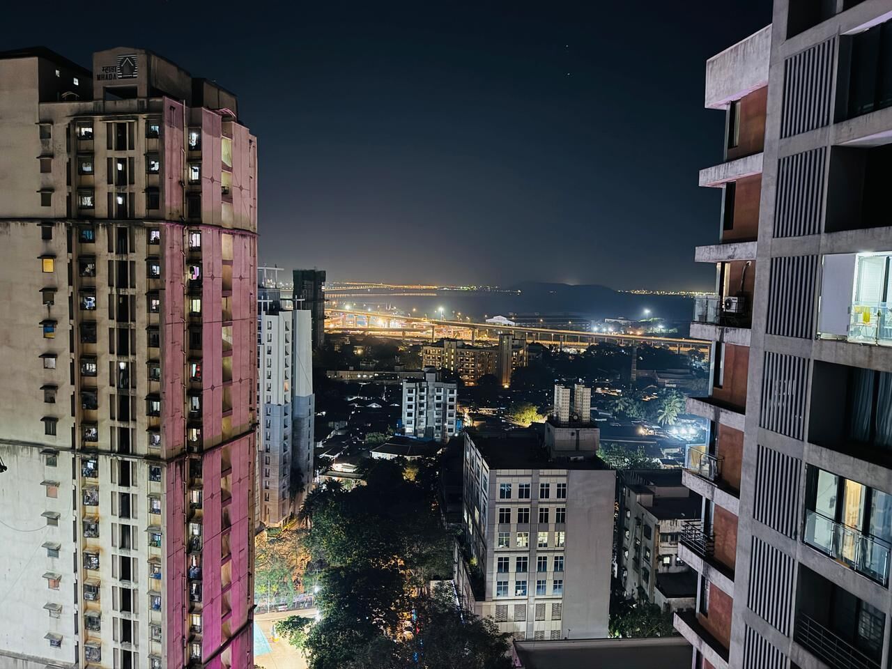 A nighttime cityscape with high-rise buildings, one with a pink facade and another with a white facade.