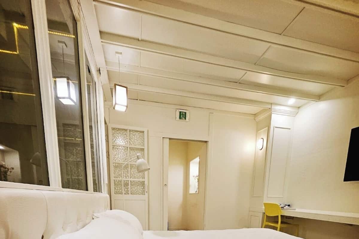 A hotel room with a large bed, a bedside table with a lamp, a chair, and a TV mounted on the wall.