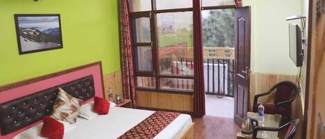 A bedroom with a bed, a wooden headboard, a window with curtains, a television, and a small table with a chair.