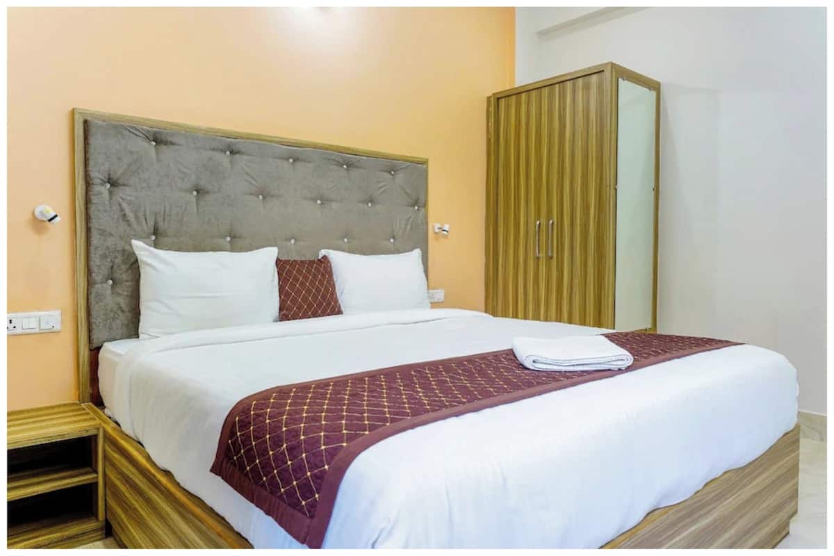 Una cama bien hecha con un cabecero acolchado, ropa blanca y una colcha color burdeos.