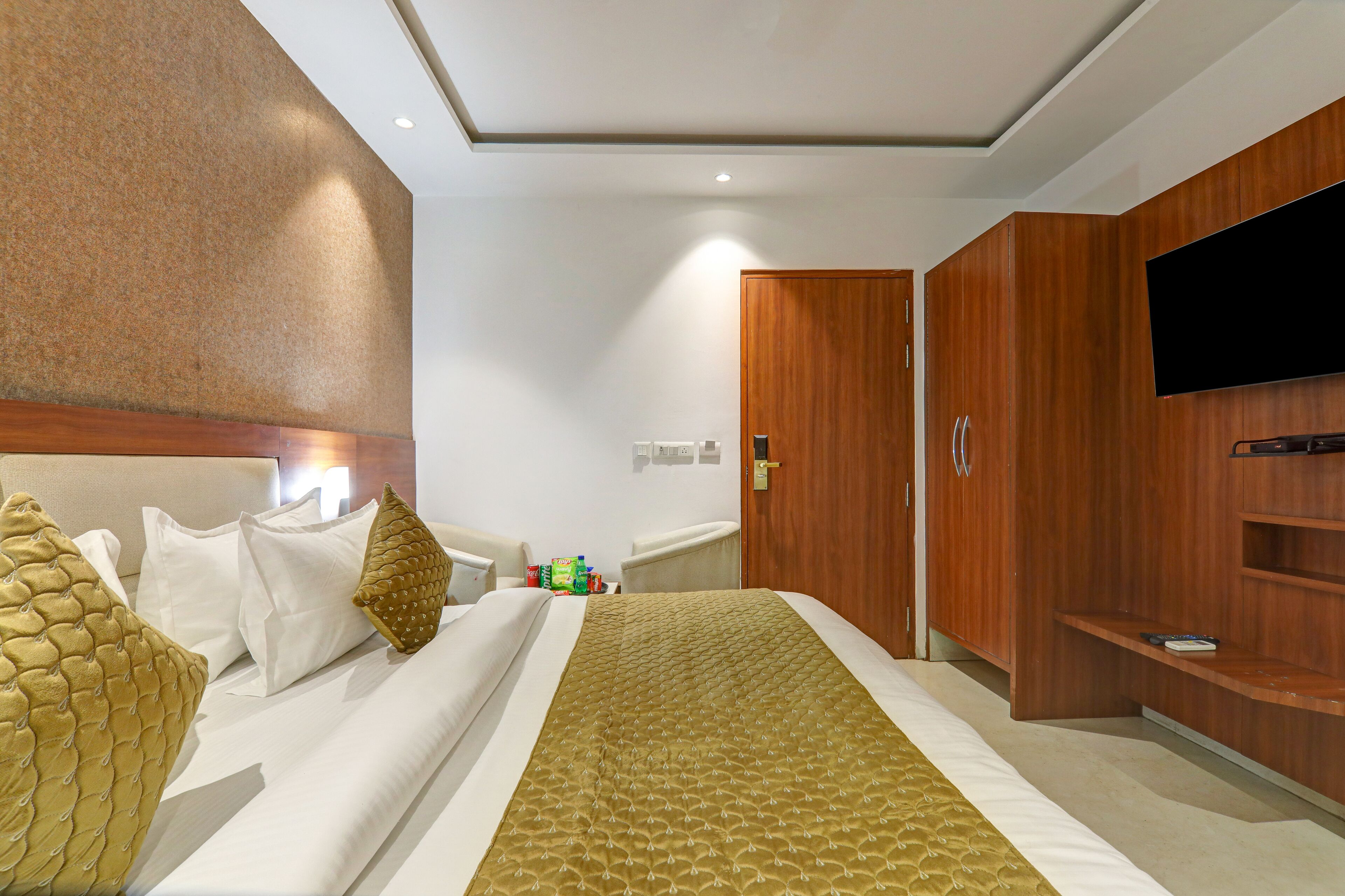 A hotel room with a bed, a TV mounted on the wall, and wooden furniture.