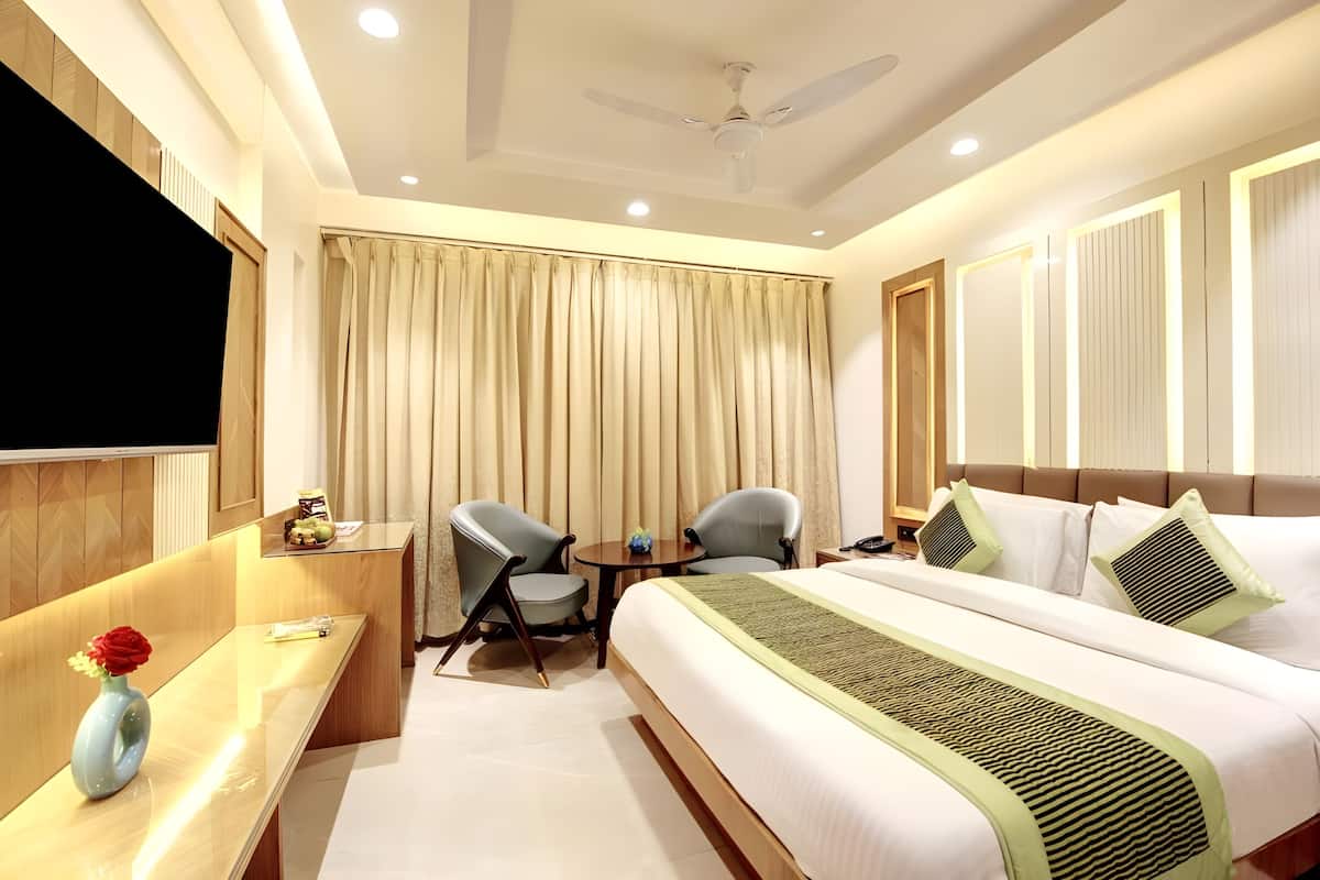 A hotel room with a bed, two chairs, a small table, a TV, and a ceiling fan.