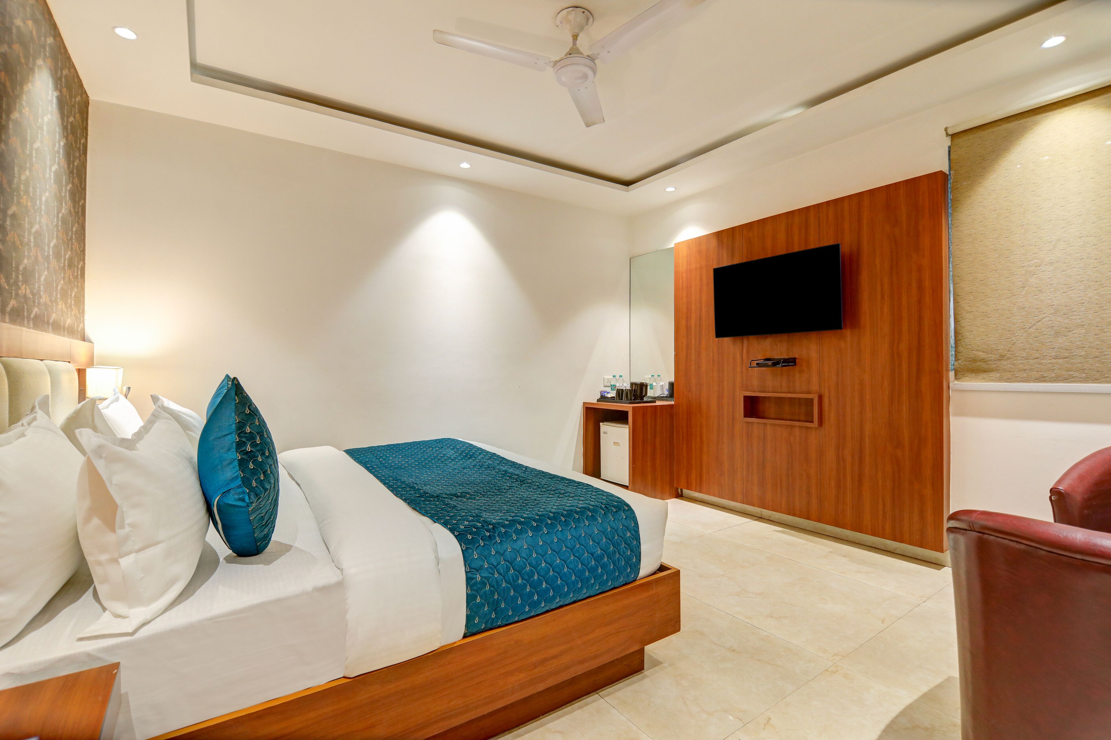 A modern hotel room with a bed, a TV mounted on the wall, a ceiling fan, and a small desk with a chair.