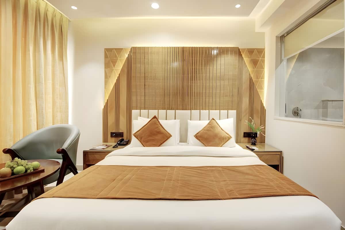 A hotel room with a large bed, a desk with a chair, a nightstand, and a window with a view.