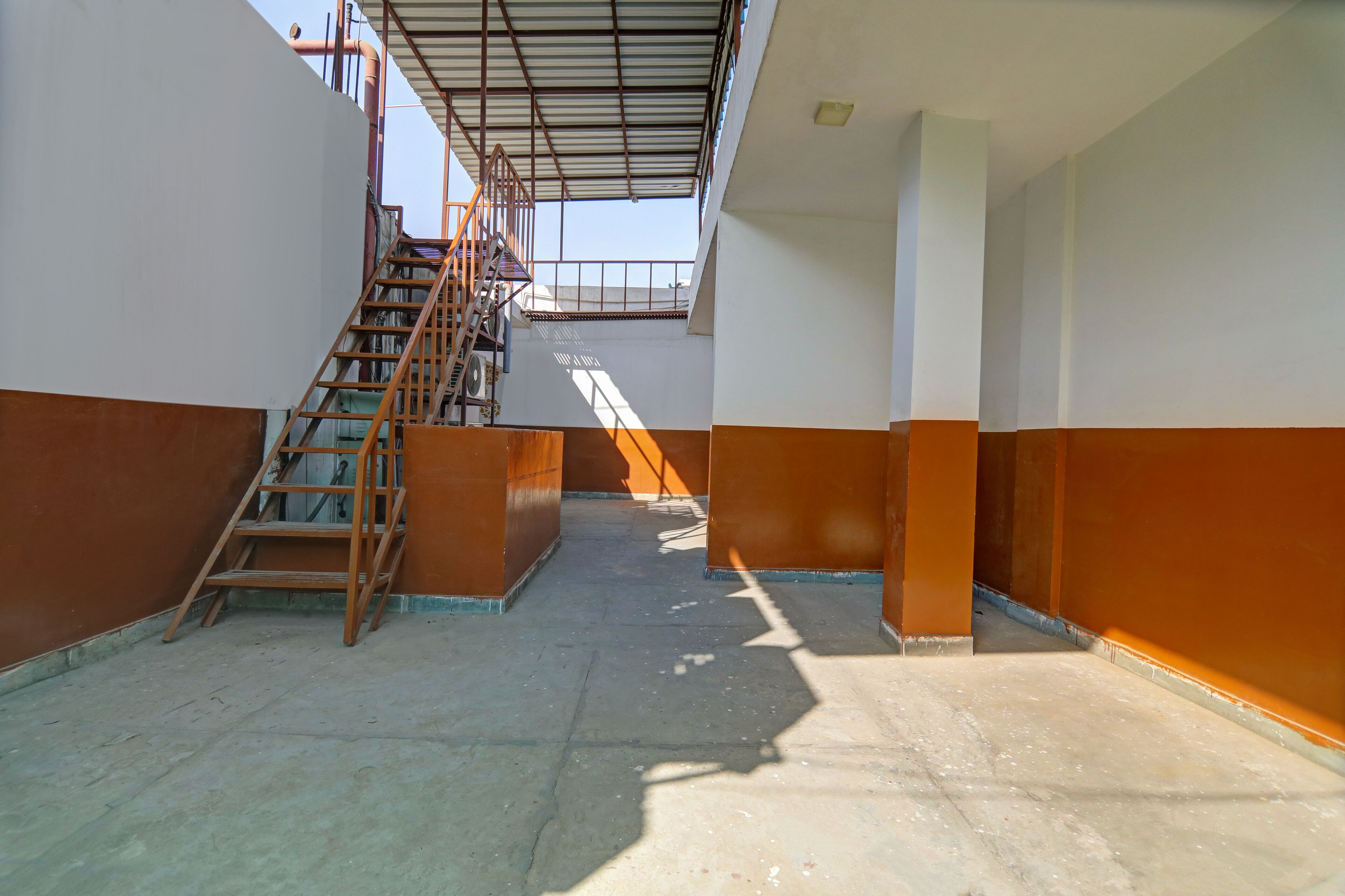 A narrow corridor with a wooden staircase leading to an upper level. The corridor has a tiled floor and walls painted in two-tone colors.