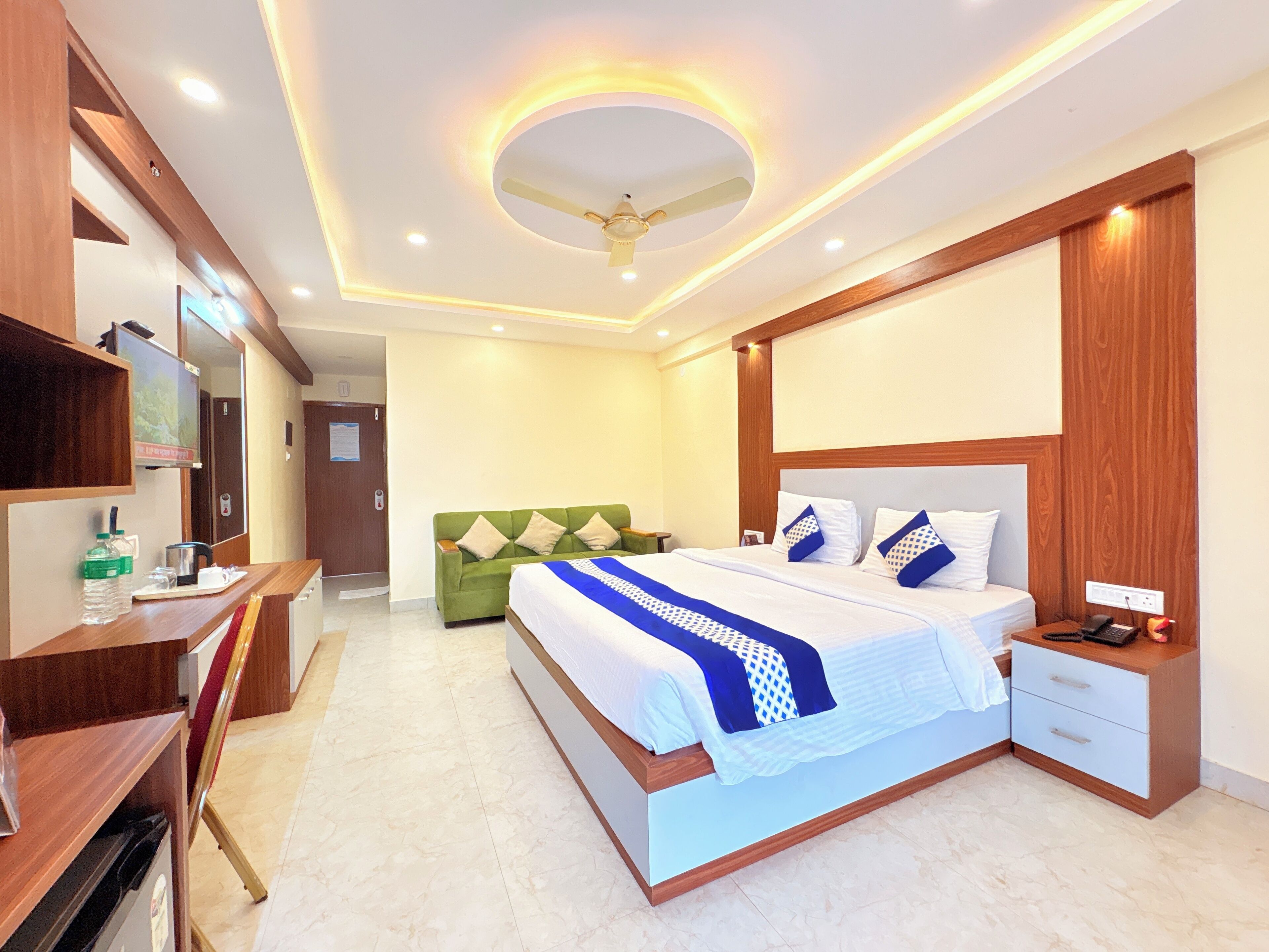 Una habitación de hotel moderna con una cama grande, un sofá verde, un escritorio con una silla y un ventilador de techo.