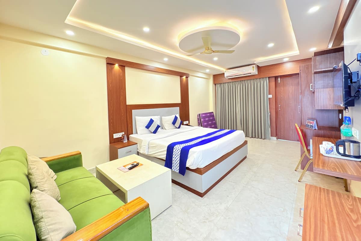 Een hotelkamer met een bed, een groene bank, een klein tafeltje, een bureau, een airconditioning en een televisietoestel.