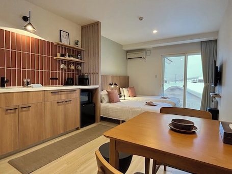 A modern hotel room with a kitchen area, a dining table, and a bed.
