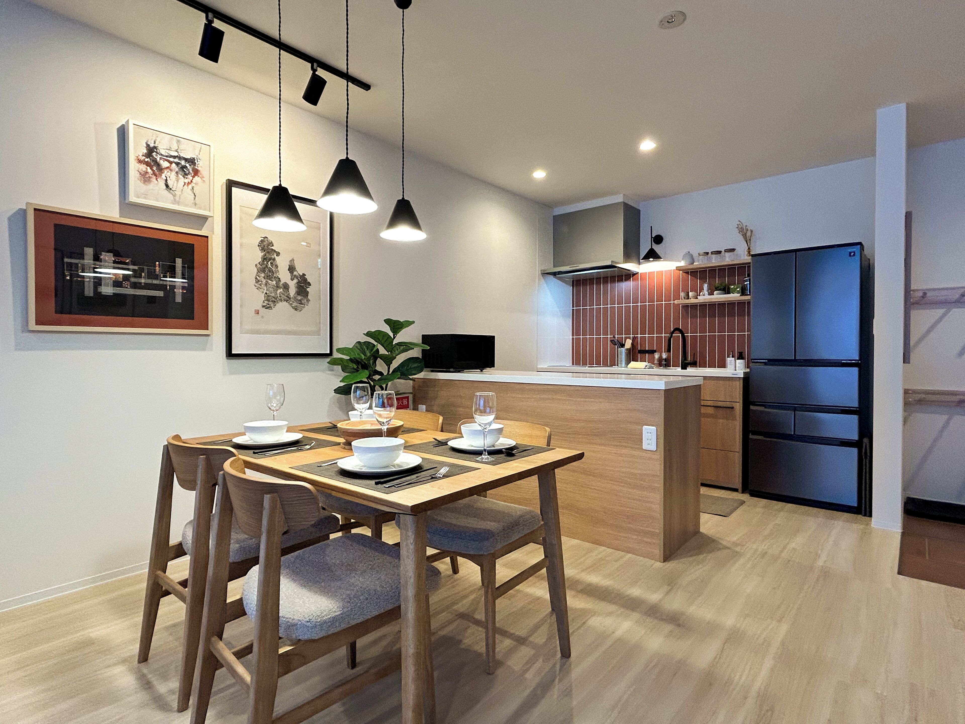 A modern kitchen with a wooden dining table, chairs, and pendant lights.