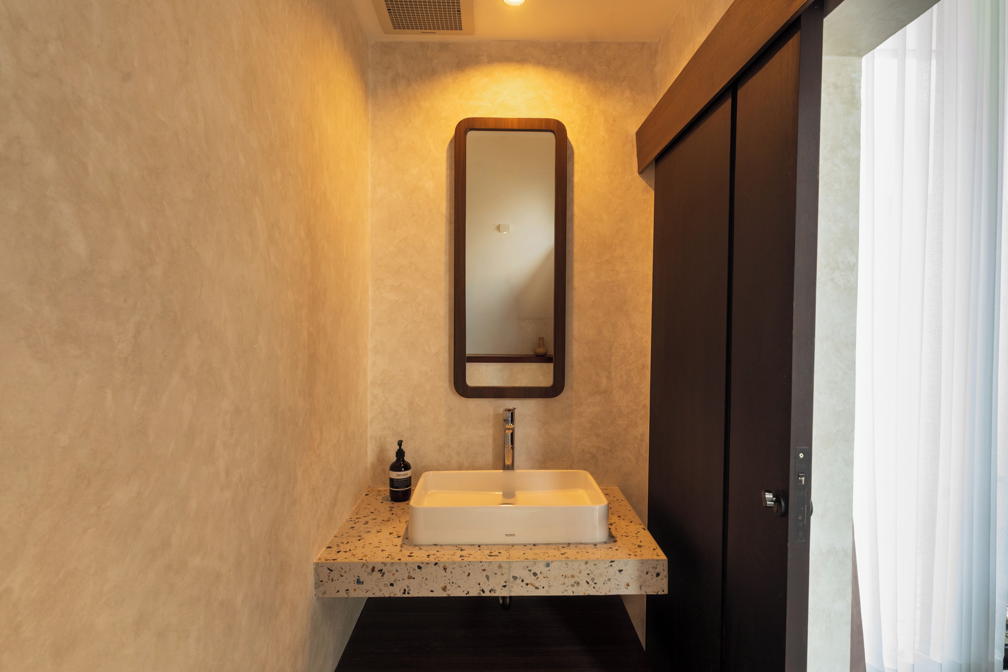 Un bagno con un lavabo rettangolare, uno specchio e una porta scura.